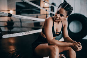 Woman Wearing Black Sports Bra And Black Shorts Sitting Near Boxing Arena Wallpaper